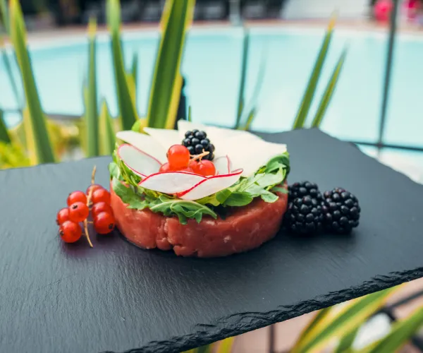 Savory appetizer with radish and berries on slate near a pool.