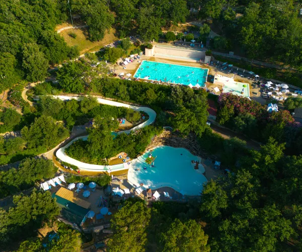 Aerial view of a water park with winding slides and two pools surrounded by trees.