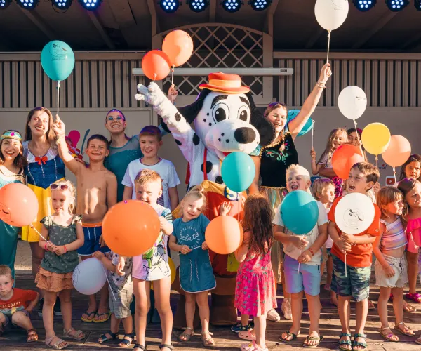 Children with balloons and a dog mascot celebrating on a stage.