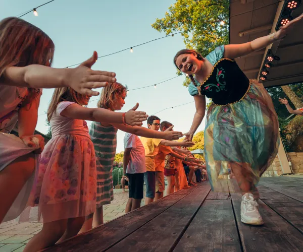 Children and adults high-fiving on a wooden stage at sunset.