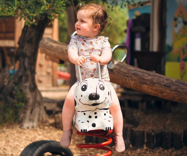Toddler on spring rocker at playground, looking to the side.