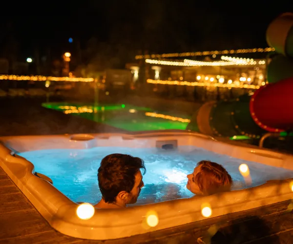 Couple relaxing in a hot tub at night, surrounded by lights.