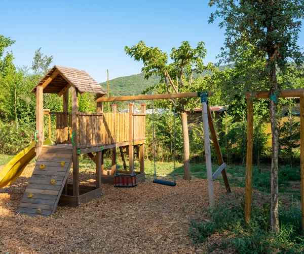Wooden playground with slide and swings in a sunny park.