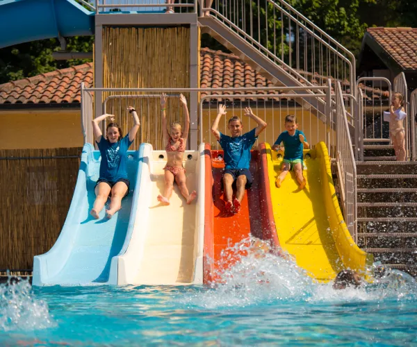 Kids sliding down colorful slides into a pool, splashing water.