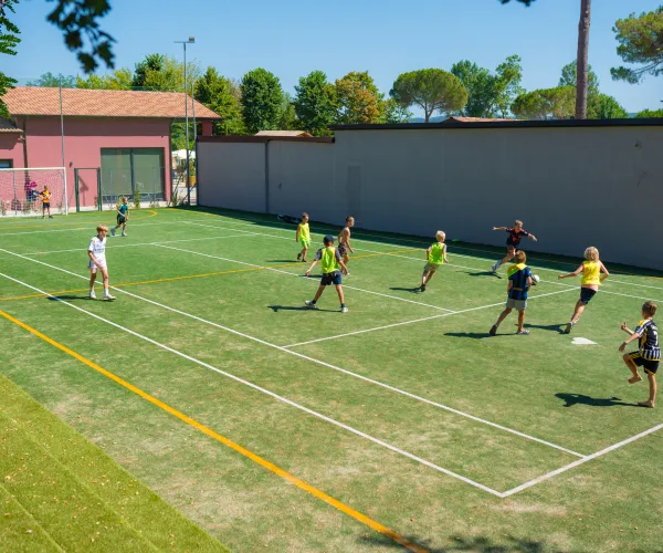 Children playing soccer on a grassy field, surrounded by buildings and trees.