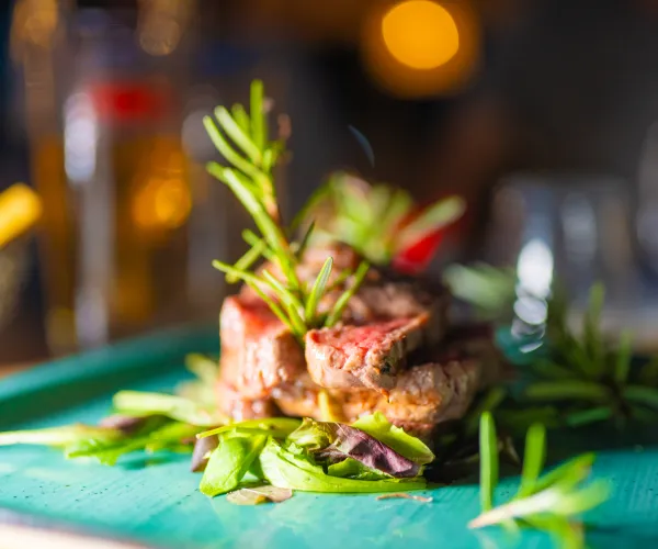 Steak garnished with rosemary on a green plate, blurred background.