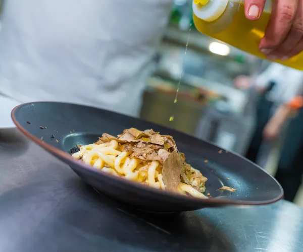 Pasta with truffle in a black bowl, being drizzled with olive oil.