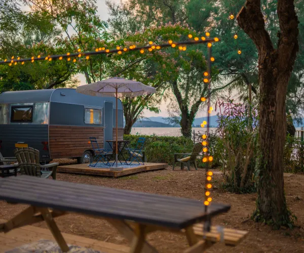 Campervan by a lake with string lights and trees at sunset.