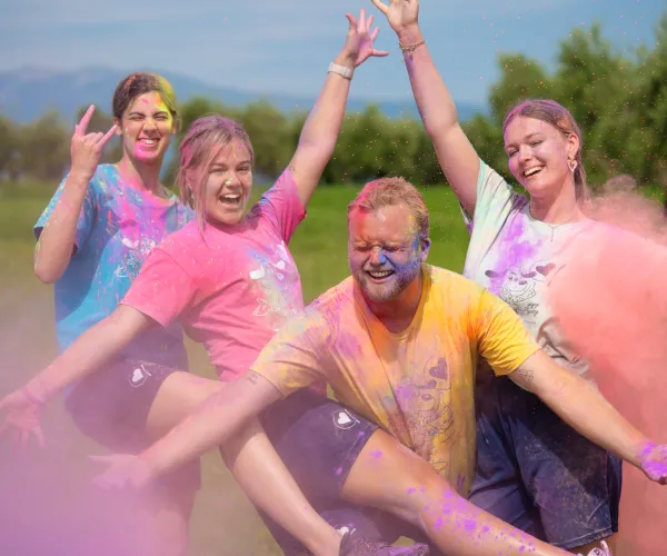 Four people outdoors celebrating with colorful powder on their clothing and faces.