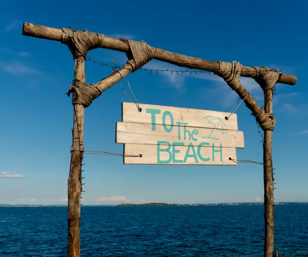 Beach sign on wooden frame against blue sky and sea.