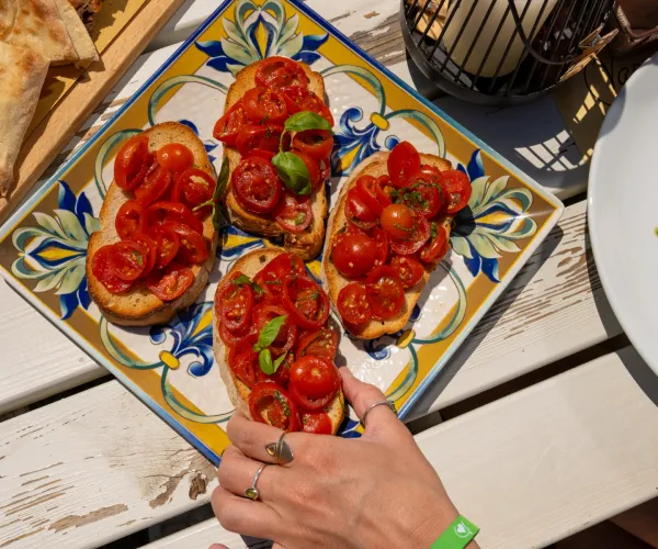 Bruschetta with tomatoes on a colorful plate, a hand reaching for a piece.