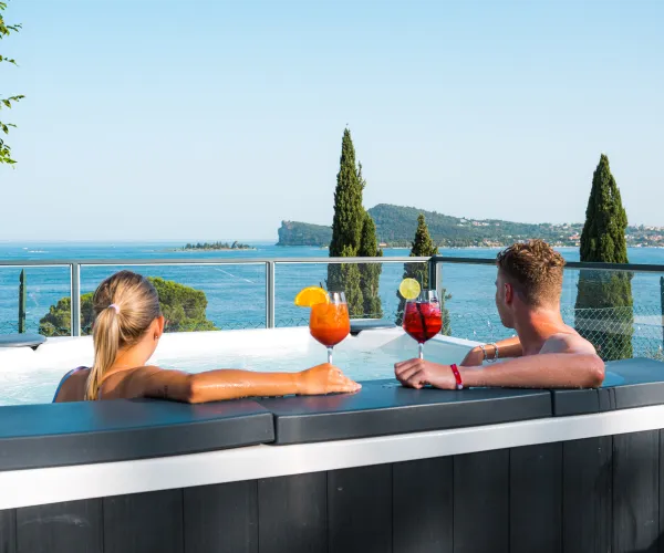 Couple relaxing in a hot tub with cocktails, overlooking a scenic lake and trees.