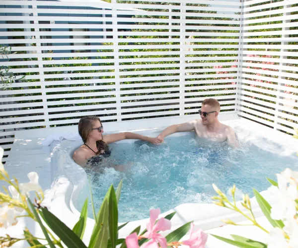 Couple relaxing in a garden hot tub, surrounded by white flowers and a privacy screen.