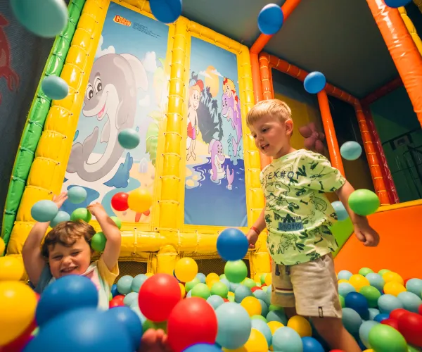 Kids playing in a colorful ball pit with a mural background.