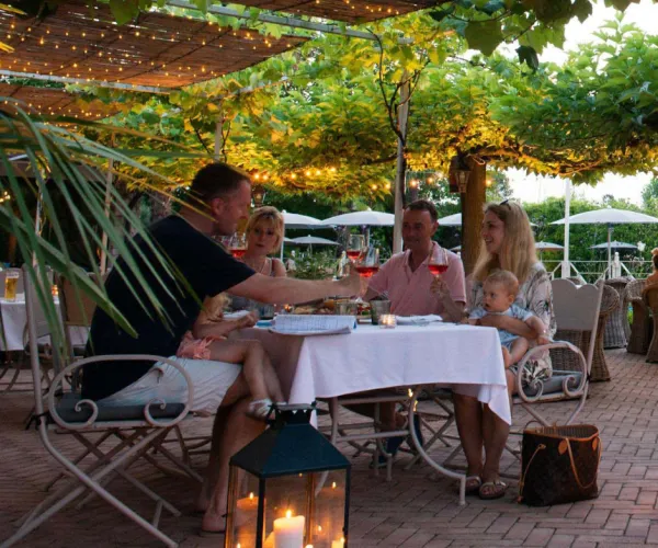 Family dining outdoors, under string lights, enjoying drinks and conversation.