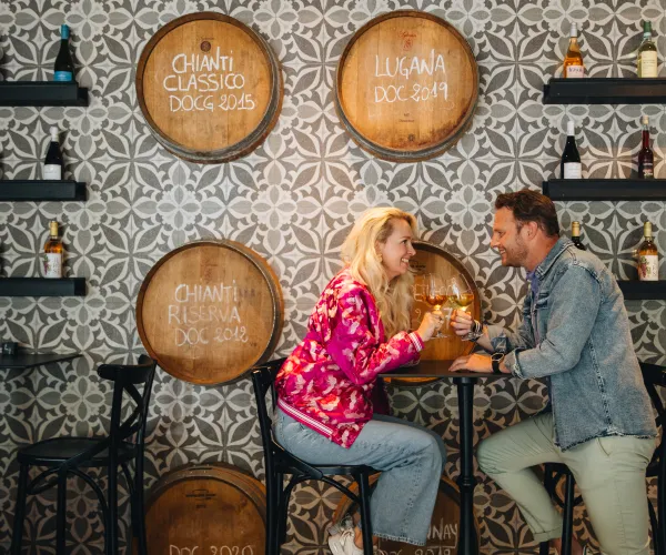 Couple enjoying drinks at a bar with wine barrels on the wall.