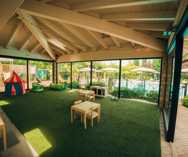 Spacious playroom with tables, chairs, and a tent, overlooking a pool area.