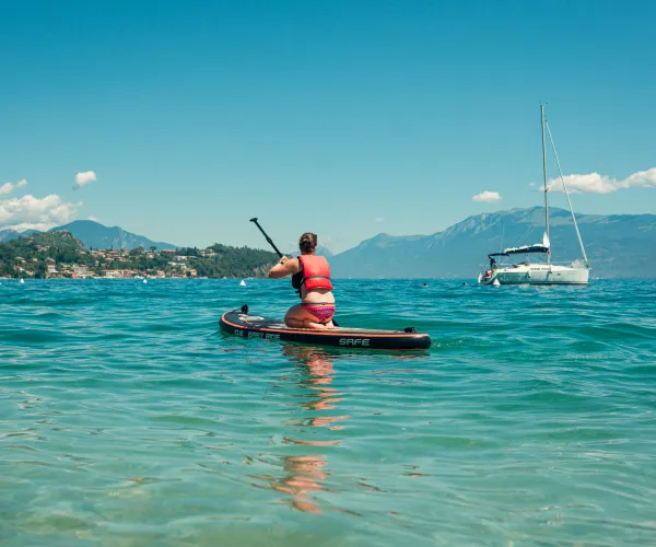 Person paddleboarding on a lake with a sailboat in the background.