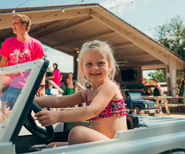 Child smiling while sitting in a toy car outdoors.