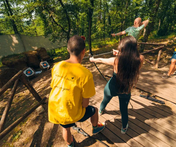 Group enjoying archery in a sunny wooded area.