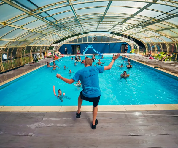 Covered pool with people swimming and a man jumping in.