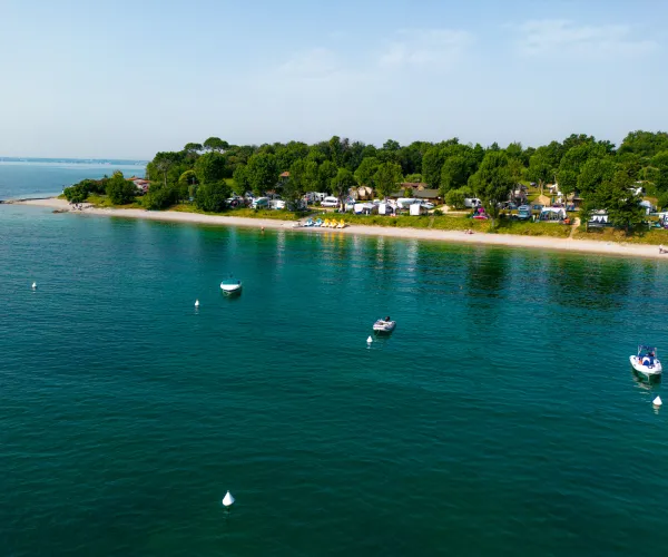 Coastal campsite with calm waters and several anchored boats.
