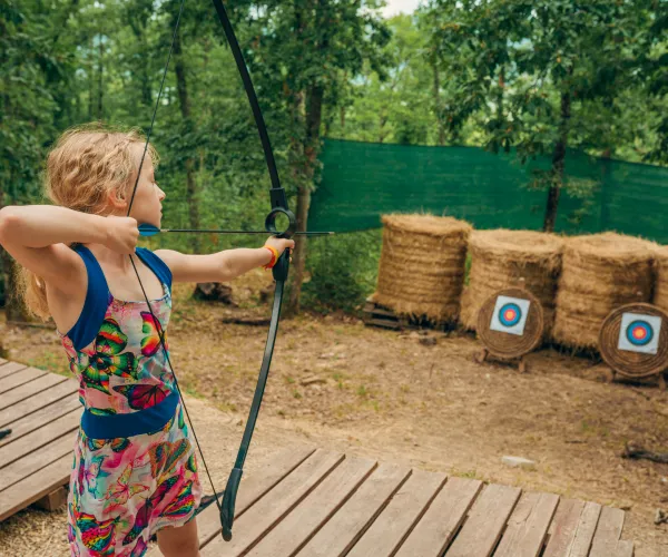 Child aiming a bow at archery targets outdoors.