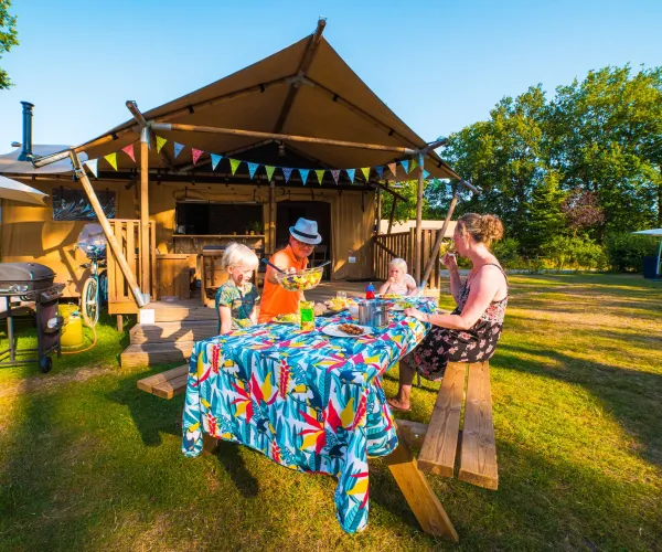 Family enjoying a picnic at a colorful table outside a wooden hut.