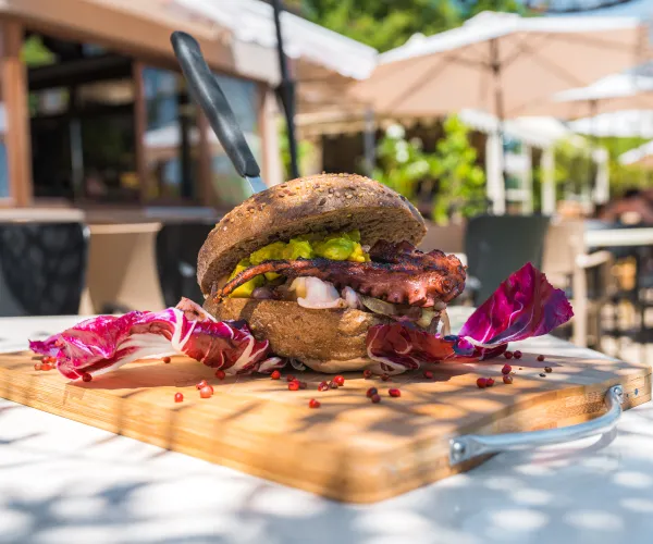 Burger with octopus tentacles on a wooden board outdoors.