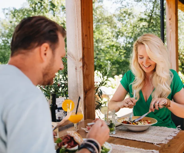 Two people enjoying a meal at an outdoor table on a sunny day.