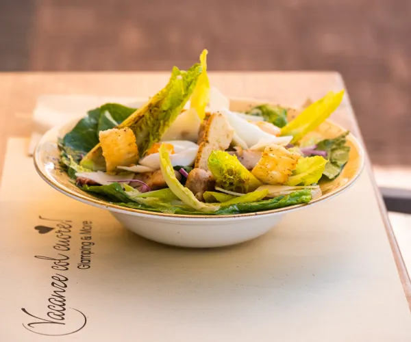 Caesar salad on a table with greens, croutons, and parmesan shavings.