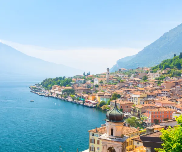 Sunny coastal town with colorful buildings, mountains, and blue water.