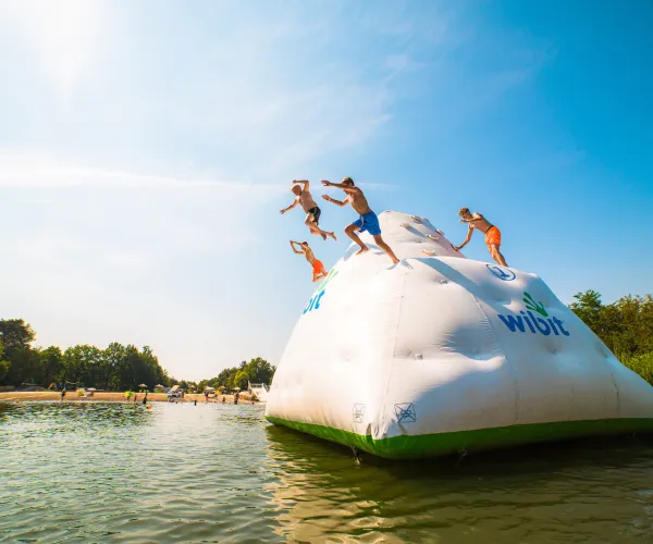 Teens jumping off an inflatable iceberg in a sunny lake.