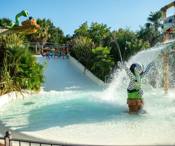 Water slide with splash zone, surrounded by trees and playful sculptures.