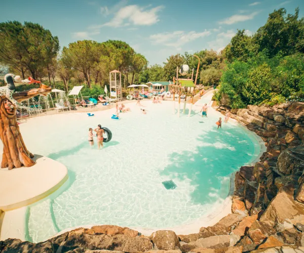 Tropical pool with people swimming, surrounded by trees and rocks.