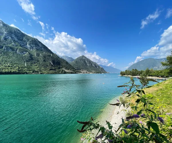 Mountainous lake landscape under a bright blue sky with fluffy clouds.