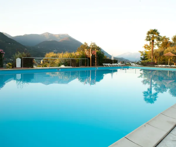Outdoor pool reflecting mountains at sunset, surrounded by trees and lounge chairs.