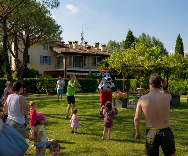 Adults and children gather on a grassy lawn, with trees and a house in the background.