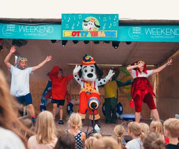 Colorful kids' stage show with performers in costumes, surrounded by a crowd of children.