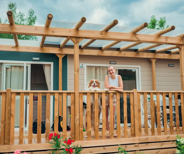 Woman and dog on a wooden porch, with flowers in the foreground.