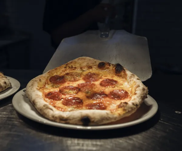 Pepperoni pizza on a plate under dim lighting.
