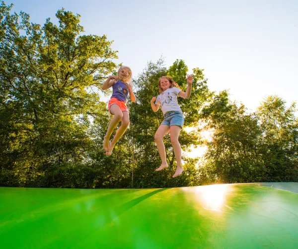 Kids jumping on a green inflatable pad, trees in the background.