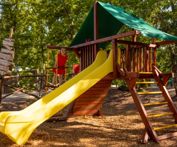 Playground with wooden structure and yellow slide under trees.