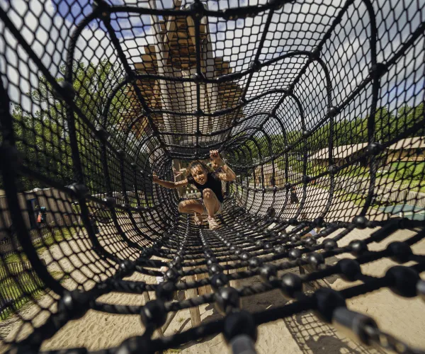 Children playing in a net tunnel, sunlight casting shadows over them.