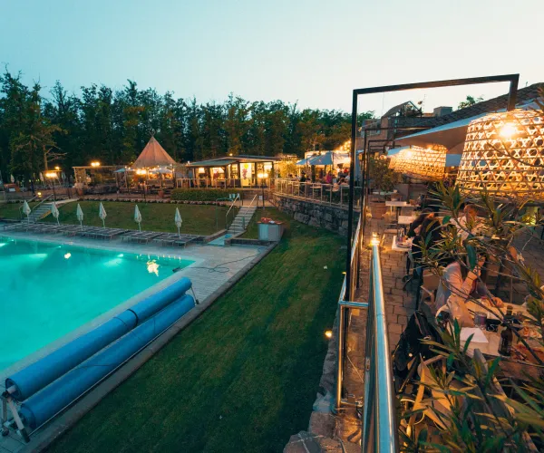 Outdoor pool area at dusk with glowing lights and trees in the background.
