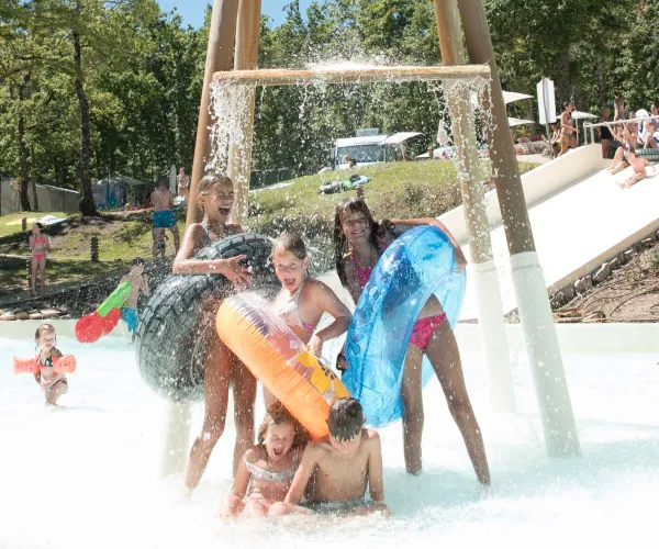 Children playing under a water feature at a sunny outdoor water park.
