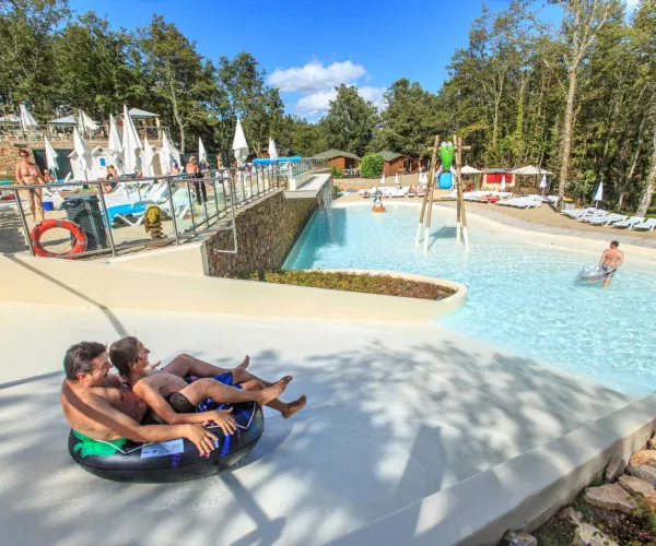 People relaxing on tubes by a sunny water park pool.