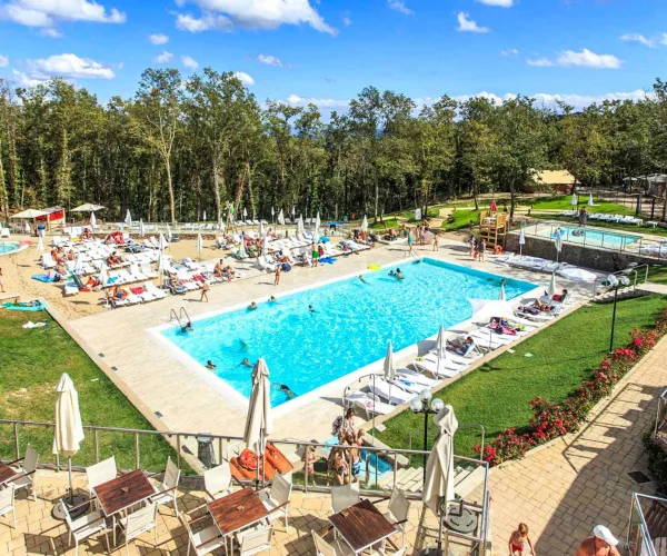 Outdoor pool scene with loungers, umbrellas, and people enjoying a sunny day.