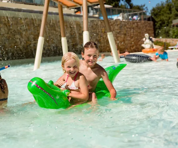 Children on green inflatable float in a sunny pool.