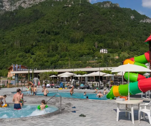 Pool area with waterslide, people swimming, and green mountains in the background.